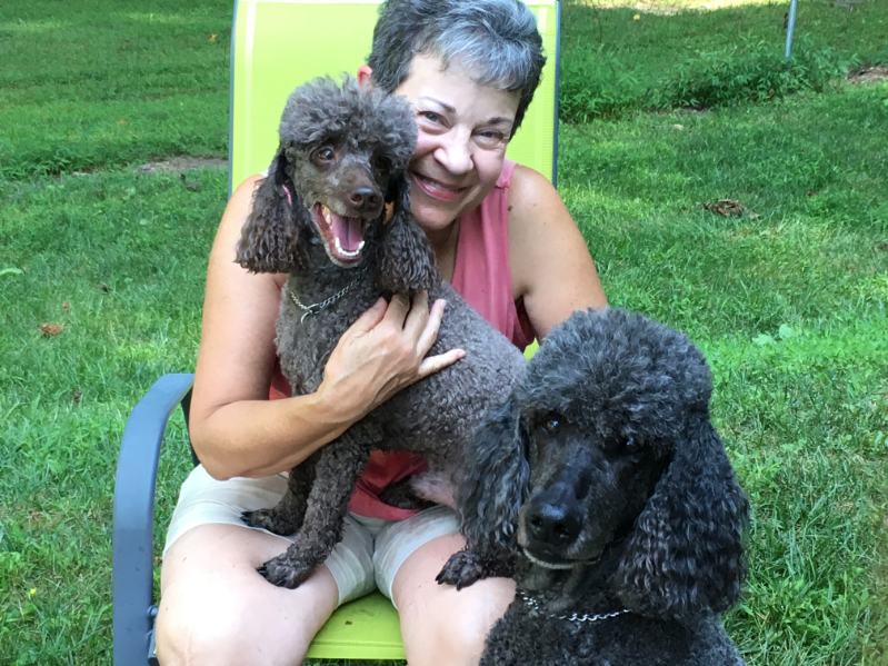 Elice cuddling two poodles in the yard
